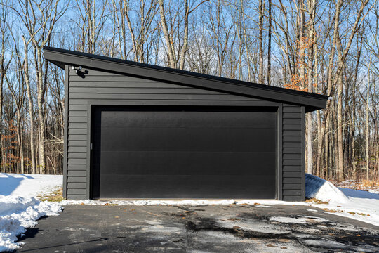 Modern black garage with slanted roof in winter forest setting
