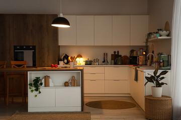 Interior of kitchen with counters, utensils and glowing lamps in evening