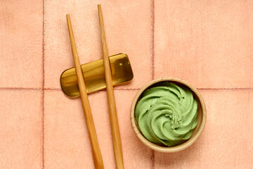 Bowl with wasabi paste and chopsticks on beige tile background