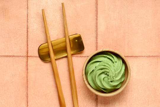 Bowl with wasabi paste and chopsticks on beige tile background