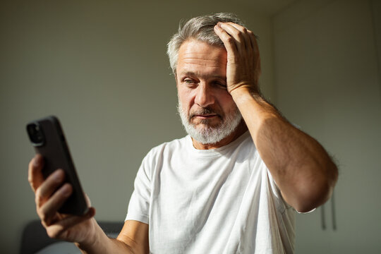 Worried senior man looking at smartphone at home