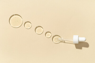 Pipette with drops of cosmetic oil on beige background