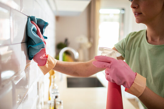 Person cleaning kitchen tile backsplash with spray