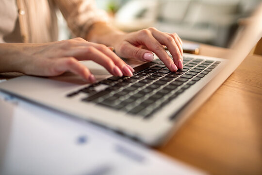 Close-up of woman's hands typing on laptop at home