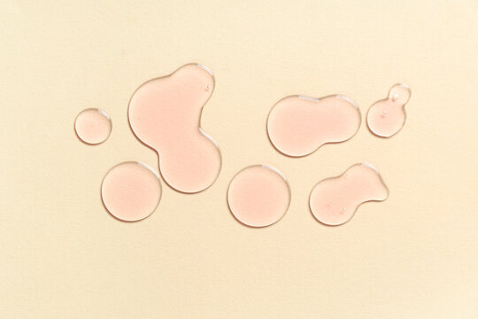 Drops of pink cosmetic oil on beige background
