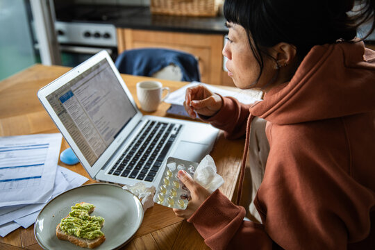 Woman taking medicine while working from home at kitchen table
