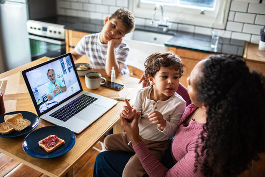 Mother and children having telehealth visit in home kitchen