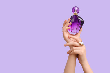 Female hands with purple bottle of perfume on lilac background