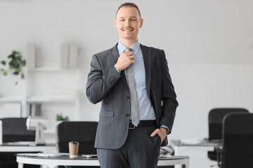 Fototapeta premium Portrait of handsome businessman fixing necktie in office