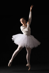 Young ballerina in tutu dancing on black background