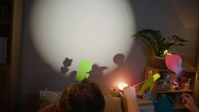 Handheld shot of loving Caucasian family of three creating shadow puppets together, enjoying playful bonding moment