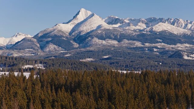 Winter view of the iconic Kriv&aacute;ň peak in the High Tatras, Slovakia, rising above dense evergreen forest. Snow covered alpine mountains under clear blue sky, calm and powerful natural scenery.