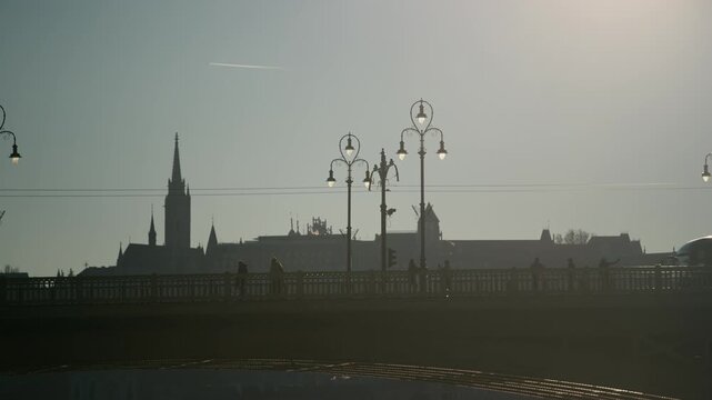 Traffic And Pedestrians On Margaret Bridge In Budapest, Hungary At Dusk, With Church Spire Silhouetted In Hazy Background. slow motion