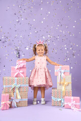 Fototapeta premium Cute little girl with gift boxes and confetti on lilac background. Birthday celebration