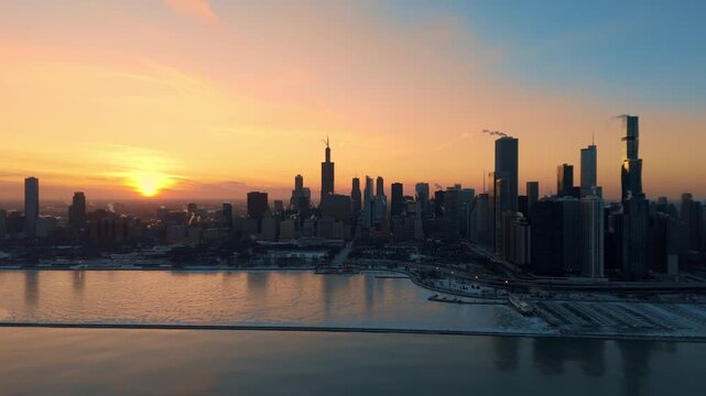 Drone view of downtown Chicago skyline at sunset during winter. The surface of Lake Michigan as subzero temperatures create frozen patterns along the shoreline