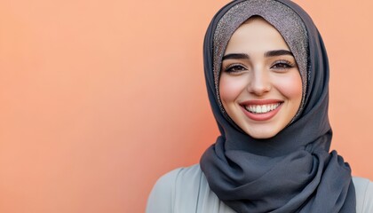 Young adult woman wearing a shimmering head covering smiles warmly against a solid colored background