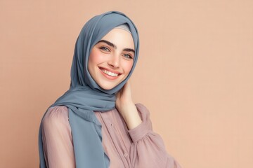Young woman wearing a muted blue head covering offers a genuine, radiant smile against a plain background.