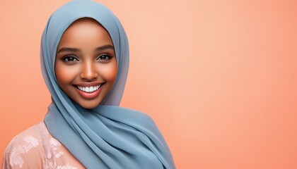 Radiant young woman wearing a light blue head covering smiles brightly against a soft coral background