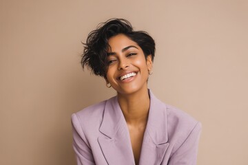 Young woman with dark, short hair beams brightly while wearing a light purple blazer against a plain background.
