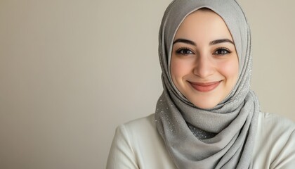 Young woman with a bright smile wearing a sparkling gray head covering against a neutral background