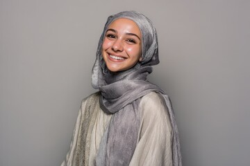 Young woman wearing a shimmering gray headscarf smiles warmly against a neutral background