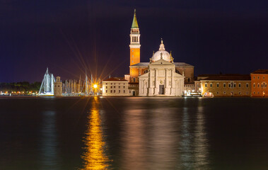 Obraz premium The illuminated facade and bell tower of San Giorgio Maggiore Church in Venice, Italy are reflected in the water under a dark night sky.