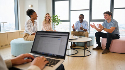 Obraz premium Diverse young professionals in casual office attire having a lively discussion and clapping hands during a meeting in a bright modern workspace with large windows and natural light.