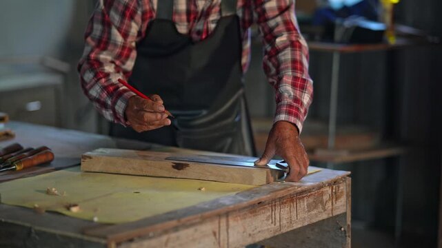 Skilled carpenter marking a wooden plank with a pencil in a workshop, demonstrating craftsmanship and dedication to woodworking and artistry.