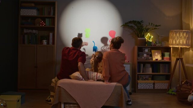 Back view shot of unrecognizable family sitting on bed and playing shadow puppets, creating story and bonding moment