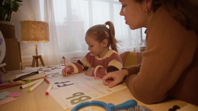 Brunette mother explaining rules of spelling while helping her little daughter with homework