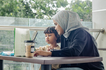 An Indonesian Muslim mother and her daughter watching a video on a tablet at a coffee shop