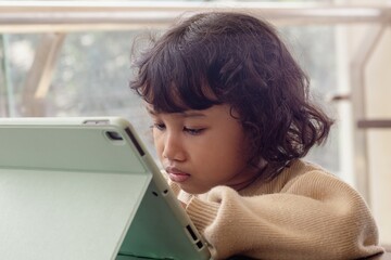 A little Indonesian girl playing games on a tablet at close range