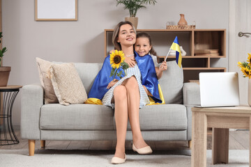 Obraz premium Cute little girl and her mother with Ukrainian flags and sunflower at home