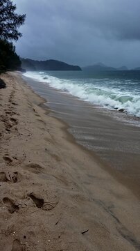 Vertical video of Pantai Cenang Beach in Langkawi, Malaysia during a stormy rainy day. Dark clouds, falling rain, and rough sea create a dramatic tropical coastal atmosphere. 