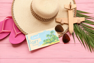 Fototapeta premium Composition with stylish beach accessories, travel gift voucher and toy plane on pink wooden background