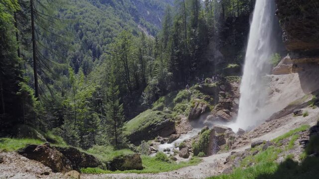 A stunning view of the Peričnik Waterfall plunging down a rocky cliff in the Vrata Valley, Slovenia. Surrounded by lush green forest.