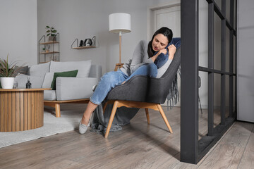 Fototapeta premium Depressed young woman with pillow sitting in armchair at home