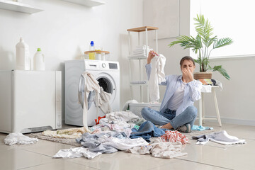 Displeased young woman with smelly laundry near washing machine at home