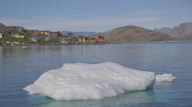 An iceberg floating in the bay of Kulusuk, a small village in Greenland, with its typical colorful Nordic houses in the background. Similar footage available in my portfolio.