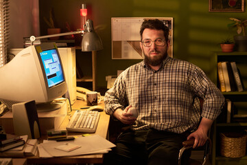 Portrait of Caucasian man with beard sitting at cluttered desk holding baseball, looking into...