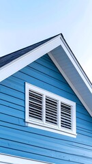 Fototapeta premium Blue house exterior with white trim and attic vent, clear sky background.