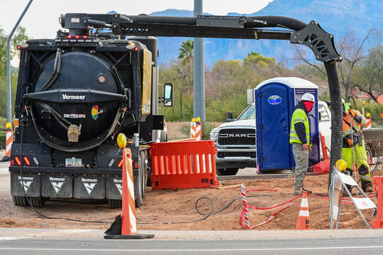 Vacuum excavation truck and crew installing curb and street infrastructure at new retail development site, representing road construction operations, underground utility access, and commercial project