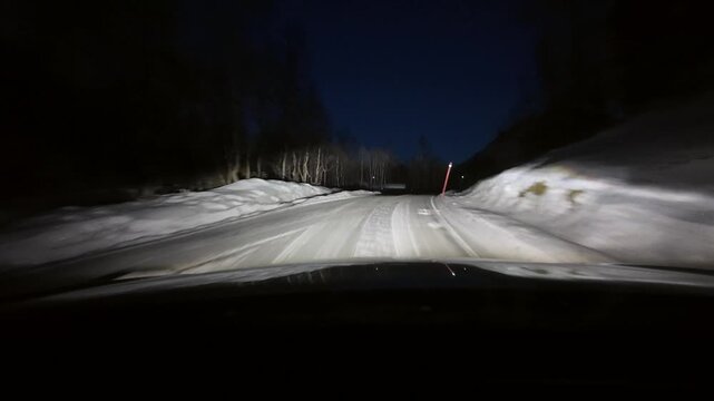 Dashboard camera view from a white sports utility vehicle driving through a winter wonderland at night.