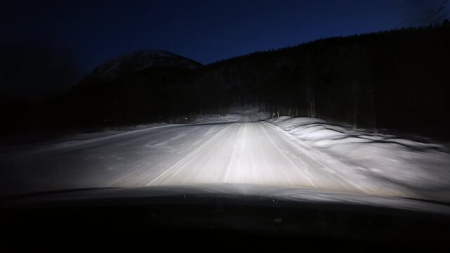 Dashboard camera view from a white sports utility vehicle driving through a winter wonderland at night.