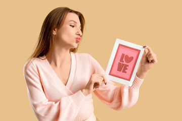 Beautiful young woman holding greeting card with word LOVE and heart on beige background....