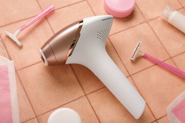 Fototapeta premium Modern photoepilator with wax strips, razors and cosmetic products on pink tile background