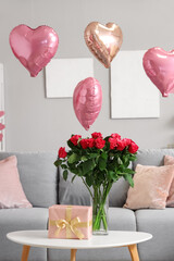 Vase with bouquet of beautiful roses and gift box on coffee table in living room. Valentine's Day...