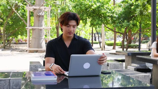 Young Asian Male Student Opens Laptop and Starts Typing Outdoors