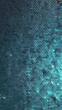 Vertical 4K video with copy space. 60 fps. Fabric for craft, sewing sea dress with scales, mermaid tail, fairy clothes. Texture of textile with blue glow shiny round sequins that shimmer in light
