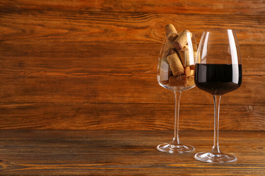 Glasses of red wine and corks on wooden background